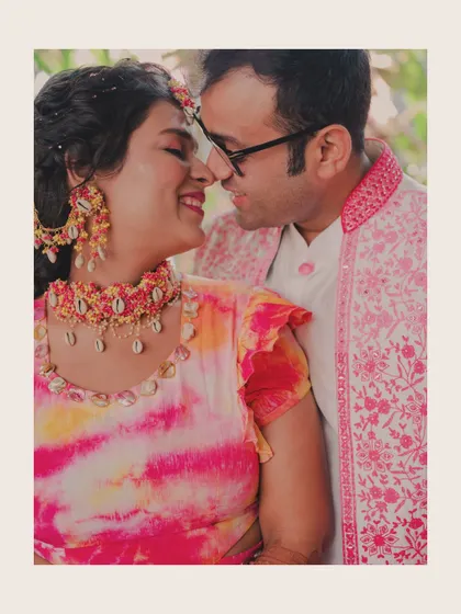 An intimate close-up of the couple, their faces close together, smiling. The bride's colourful tie-dye outfit and shell jewelry add a unique, bohemian touch.