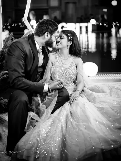 A romantic black and white photo of a couple sharing a kiss by the water on their engagement night. The lights reflecting on the water add a touch of magic.