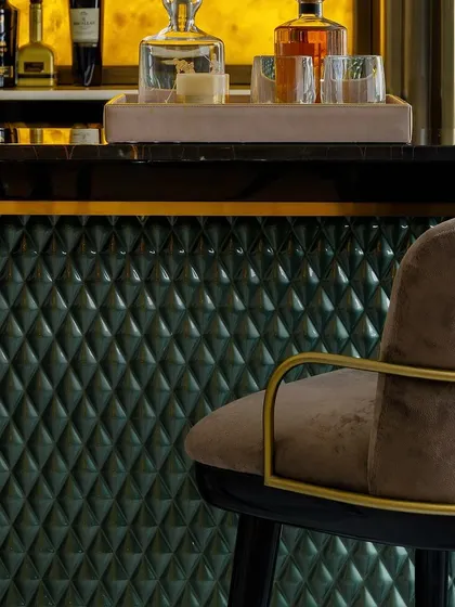 A close-up of the bar area, highlighting the quilted green leather front and the elegant, high-back bar chair. Every detail, from the glassware to the lighting, is curated to create a sophisticated experience.