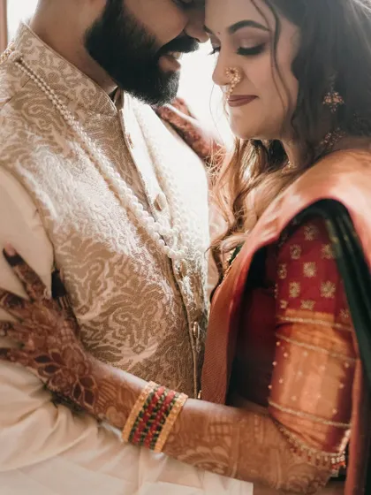 An intimate close-up focusing on their embrace. The intricate details of her saree and his jacket are beautifully highlighted.