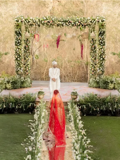 The bride's grand entrance, walking towards the groom who waits at the mandap. The long shot captures the scale and emotion of the moment.