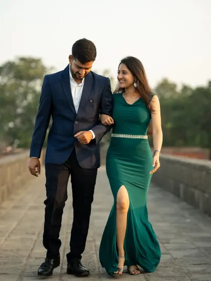 A happy couple walking arm-in-arm across a stone bridge, captured during a golden hour pre-wedding shoot.