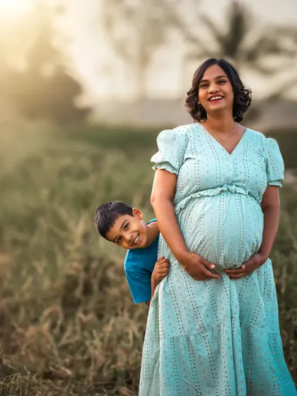 A duplicate of ID 8, this joyful outdoor family portrait shows a young boy playfully peeking out from behind his pregnant mother, with golden sunlight adding a warm glow.