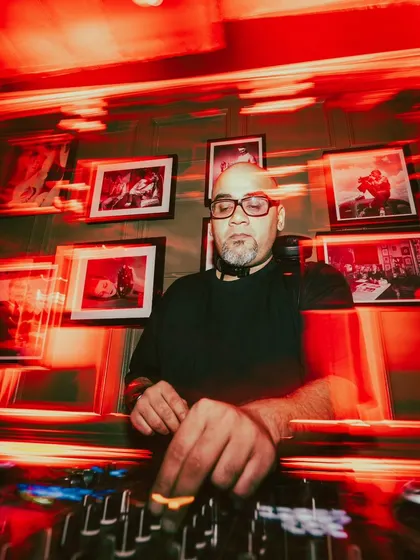The DJ, lit by the red glow of the booth, focused on the mix.