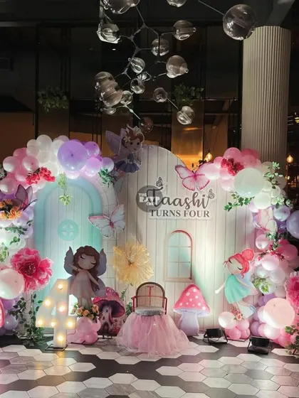 An enchanted garden theme for a 4th birthday, with a beautiful backdrop of a fairy house, whimsical mushrooms, and a balloon arch filled with flowers and butterflies.