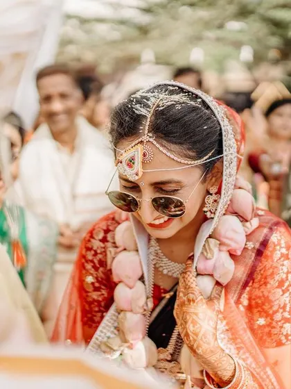 A candid moment of the bride smiling shyly during her wedding ceremony, wearing cool sunglasses.