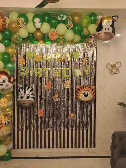 A jungle-themed birthday decoration for a home setting, using a shimmer curtain and animal foil balloons.