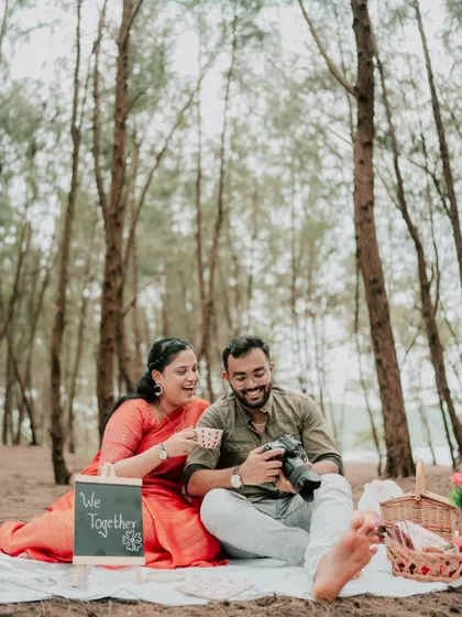 A couple sharing a laugh while reviewing photos on the camera during their pre-wedding picnic.