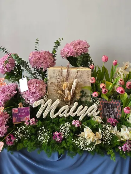 An elegant floral hamper for Maiya, featuring a bed of greenery, lush pink hydrangeas, tulips, and a personalized name in pearls.