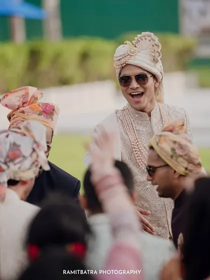 The groom, wearing sunglasses and a turban, dances with his friends during his Baraat.