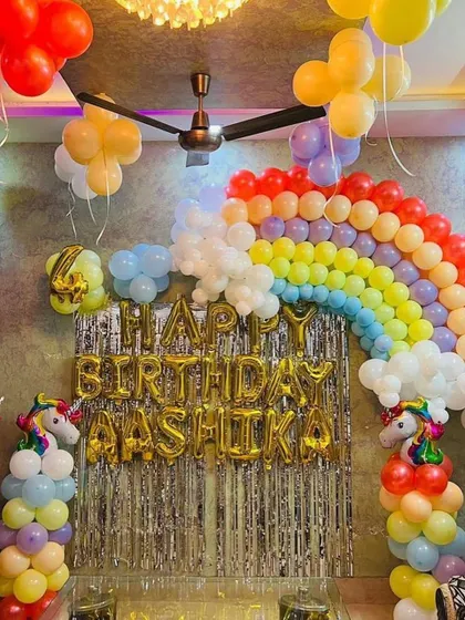 A classic Unicorn theme party at home, with a rainbow balloon arch over a silver fringe backdrop and unicorn balloon pillars.