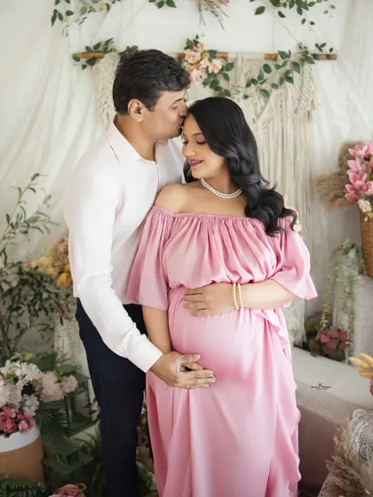 A tender kiss on the forehead speaks volumes. This intimate couple's portrait, set against a soft floral and macrame backdrop, is all about quiet love and anticipation.