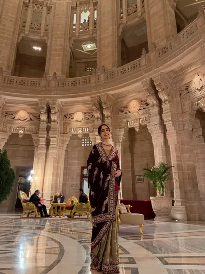 A full-length shot that captures the grandeur of both the palace and the royal velvet saree.