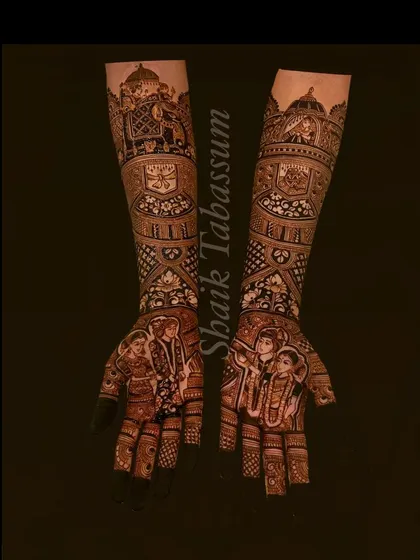 This dark-stained mehendi showcases a couple's portrait on the palms, framed by intricate patterns. The forearms feature a royal elephant procession, adding a touch of grandeur to the bridal design.