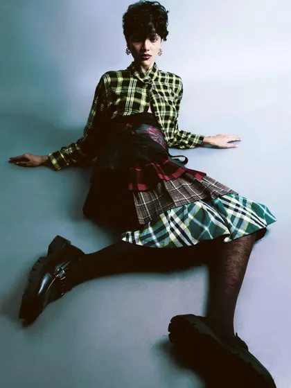 A high-angle shot of the model seated on the floor. This perspective provides a clear view of the eclectic outfit and creates a relaxed, grounded composition.
