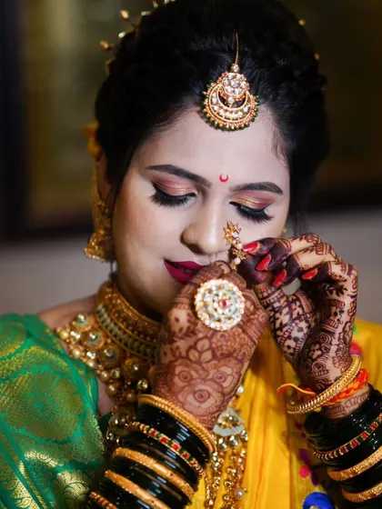 A close-up of the bride adjusting her nath, capturing the fine details of her jewelry and the rich texture of her yellow and green saree.