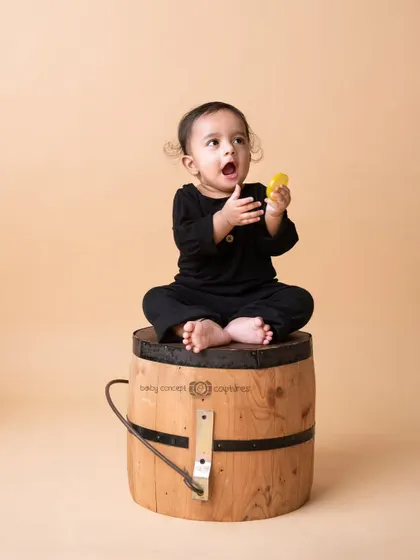 A full-body shot of a baby sitting on a barrel, capturing a moment of surprise and curiosity.