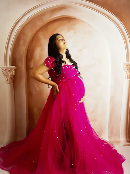 A powerful pose in a vibrant pink gown against a classic archway backdrop. The upward angle and lighting create a dramatic and statuesque look.