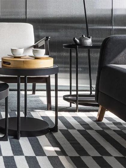 The reception area is designed with a monochrome palette, but is rich in texture. A striped rug, multi-levelled marble and metal coffee tables, and a fluted glass backdrop create a sophisticated and layered look.