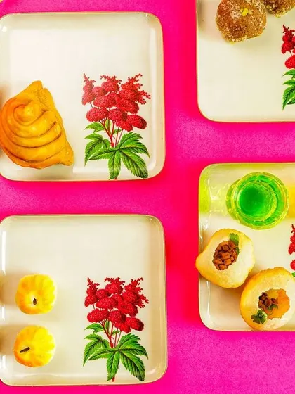 A vibrant flatlay of square plates with a floral motif, set against a bright pink background. This bold, colorful shot is perfect for social media.