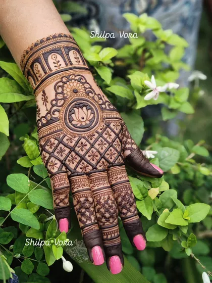 A single hand featuring the lotus mandala design, set against a natural green background.