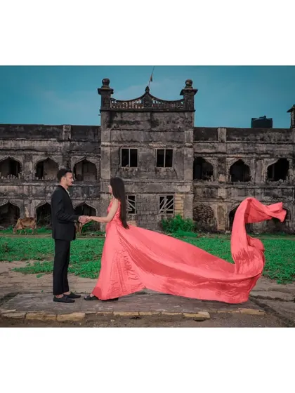 A couple shares a moment in front of a magnificent, old fort, with the bride's dramatic pink gown adding a splash of colour to the historic scene.