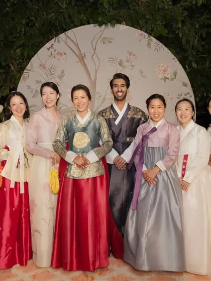 A group portrait of the wedding party dressed in colorful Hanboks, standing with the couple in front of the custom-designed ceremony backdrop.