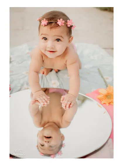 I love using creative props like this mirror to add a touch of magic to outdoor sessions. This baby girl, wearing a sweet floral headband, is fascinated by her own reflection, creating a unique and engaging portrait for her first birthday shoot.