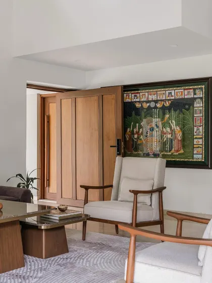 We love incorporating our clients' personal stories into our designs. In the Relic House, a traditional Pichwai painting owned by the family becomes a stunning focal point, beautifully juxtaposed with the clean lines of the modern armchair and the solid wooden door.