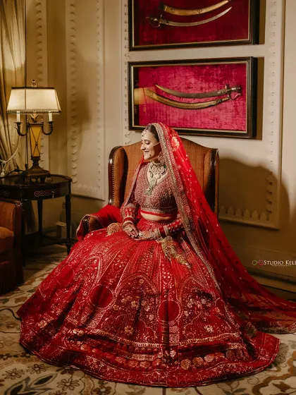 A majestic bridal portrait at the ITC Grand Bharat, with the bride seated in a stately room, her red lehenga spreading out beautifully.