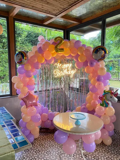 A unicorn-themed second birthday party with a circular balloon arch in pastel orange and purple.