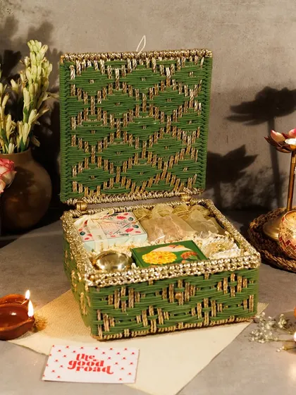 Another angle of our festive green woven hamper, showcasing the beautiful craftsmanship of the box and the curated items within, surrounded by glowing diyas.