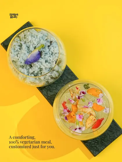 A beautifully artistic shot of my Thai Green Curry and blue jasmine rice, presented in modern glass bowls against a vibrant yellow background. The edible flowers add a touch of elegance, showing my commitment to beautiful presentation.