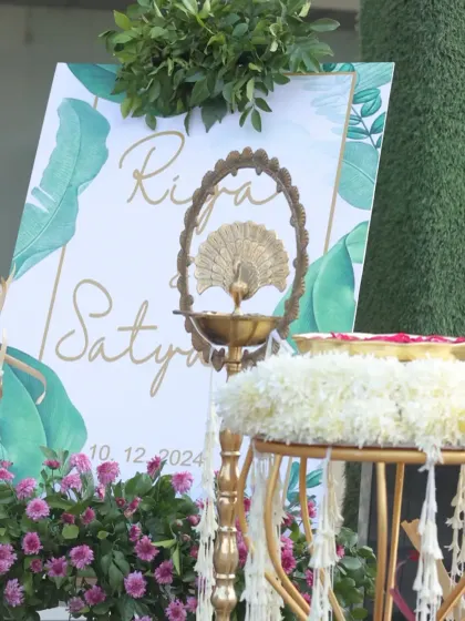 A personalized welcome sign featuring the couple's names and wedding date, with a tropical leaf design. The decor is enhanced with a traditional brass peacock lamp, blending modern and classic elements.