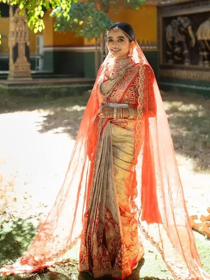 This bride is a vision in her complete bridal ensemble. The heavily embroidered blouse, matching saree border, and long, flowing veil create a look of unparalleled grandeur.
