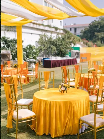 Outdoor guest seating for a Haldi function, with tables and chairs dressed in bright yellow fabric, creating a cheerful and sunny ambiance.