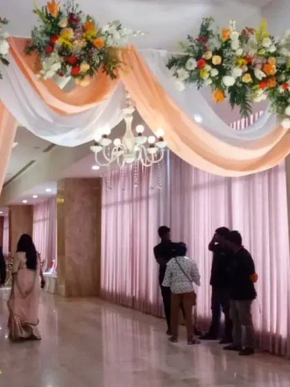 A grand entrance to a reception hall, framed by an arch of peach and white drapery and lush floral arrangements. A chandelier adds a touch of formal elegance.