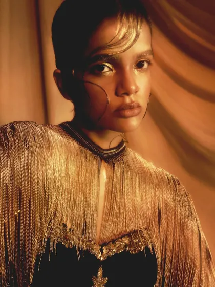 A beautiful close-up of the fringed outfit and the complementary gold makeup, highlighting the textures of the look.