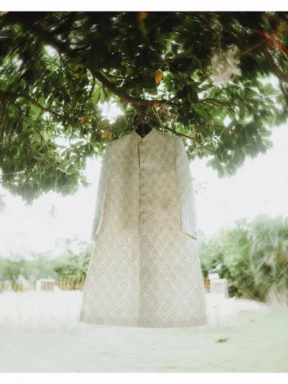 An artistic shot of the groom's sherwani hanging from a tree before the wedding.