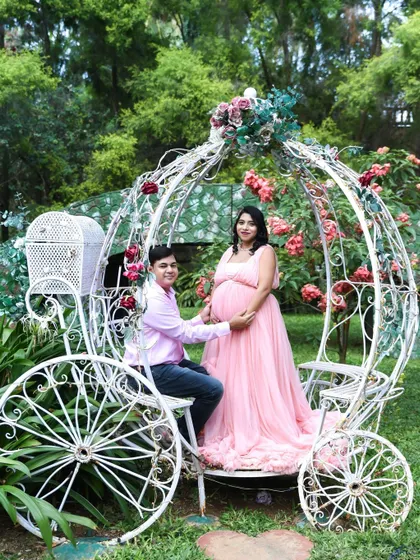 A true fairytale moment. This couple is posing in a beautiful, ornate white carriage in a garden, perfect for a princess-themed maternity shoot.