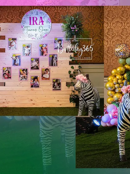 A vibrant photo showing the personalized memory wall and themed props for Ira's jungle party. The combination of the photo display and the cute zebra figures creates a perfect spot for guests to enjoy.
