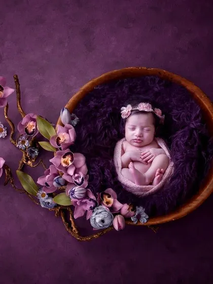 Inspired by nature, this portrait features a newborn nestled in a wooden bowl, adorned with a cascade of purple orchids. The rich color palette and organic elements come together to create a truly artistic and memorable image.