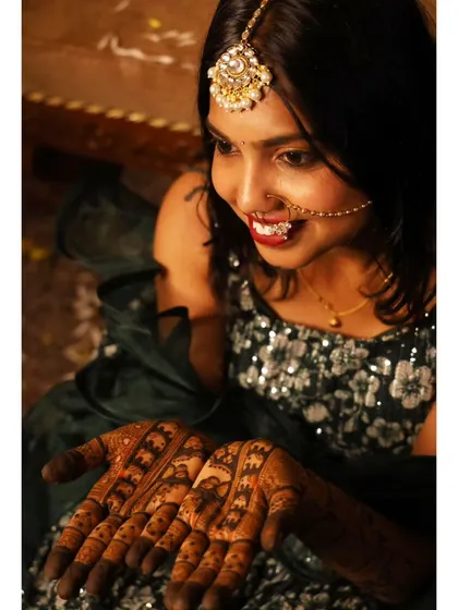 A smiling bride proudly displaying her wedding mehendi. The design is filled with traditional symbols that add deep meaning to her bridal look.