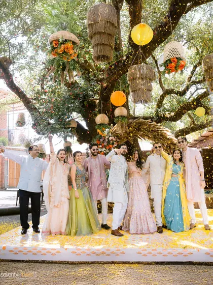 The couple with their friends and family, celebrating under a shower of flower petals at their outdoor Haldi ceremony.