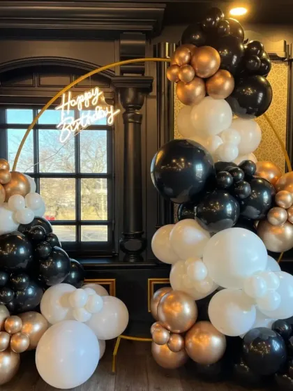 A sophisticated black, white, and bronze gold balloon arrangement on a circular frame. This elegant design with a neon sign is perfect for upscale birthday parties or corporate events.