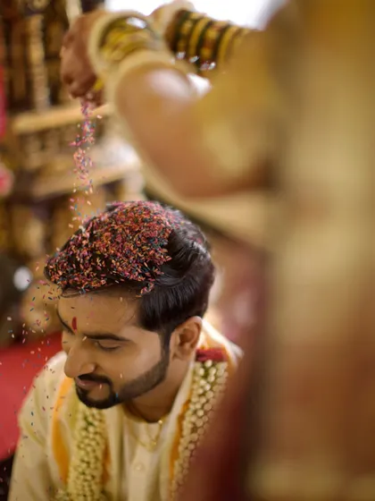 A close-up of the groom during the 'talambralu' ritual, capturing the texture of the colored rice and his serene expression.