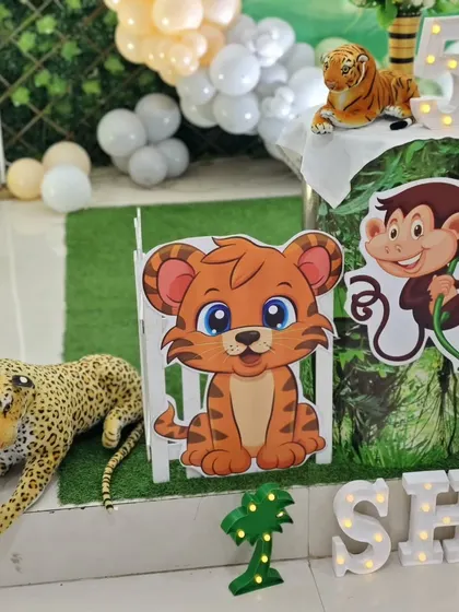 A detailed shot of a jungle-themed party with cute cartoon animal cutouts, plush toys, and marquee letters spelling the birthday boy's name.