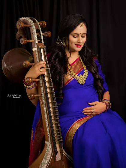 A detailed shot focusing on the mother-to-be's serene expression as she holds the Veena. The rich colors of her attire and the intricate details of the instrument are highlighted beautifully.