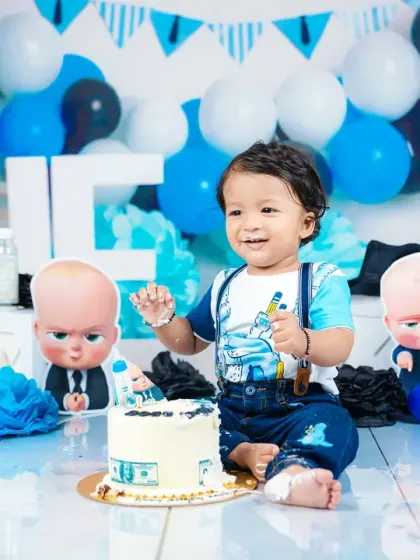 A fun and memorable "Boss Baby" themed cake smash for a first birthday. This shot captures the pure, messy joy of a baby enjoying his first taste of cake in a creative, fully-styled setup.