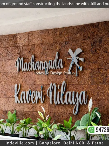 The final touch on a new landscape: a custom nameplate installed on a textured wall, framed by freshly planted peace lilies.